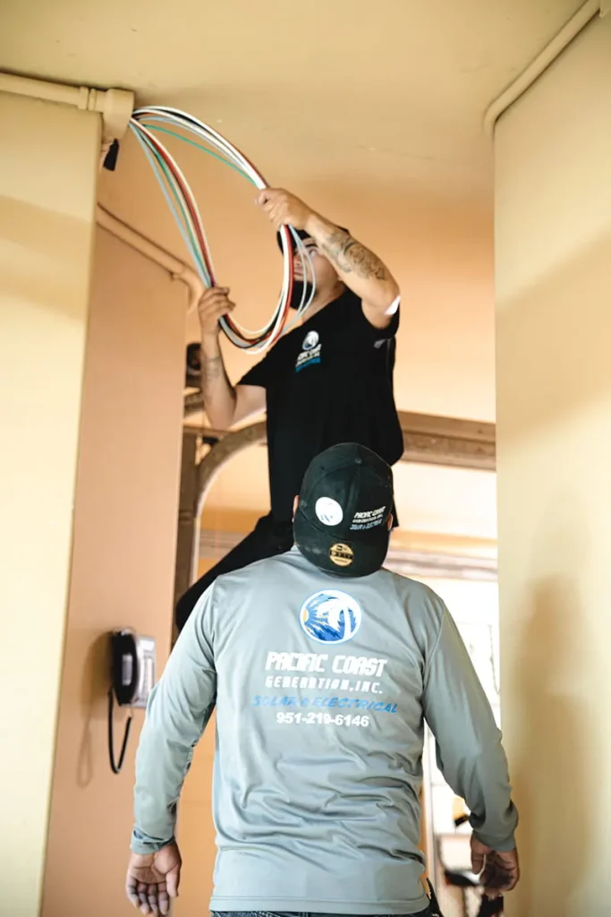 Solar installers routing electrical wiring through conduit in a residential garage
