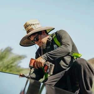 Solar technician securing a solar panel with a drill during rooftop installation