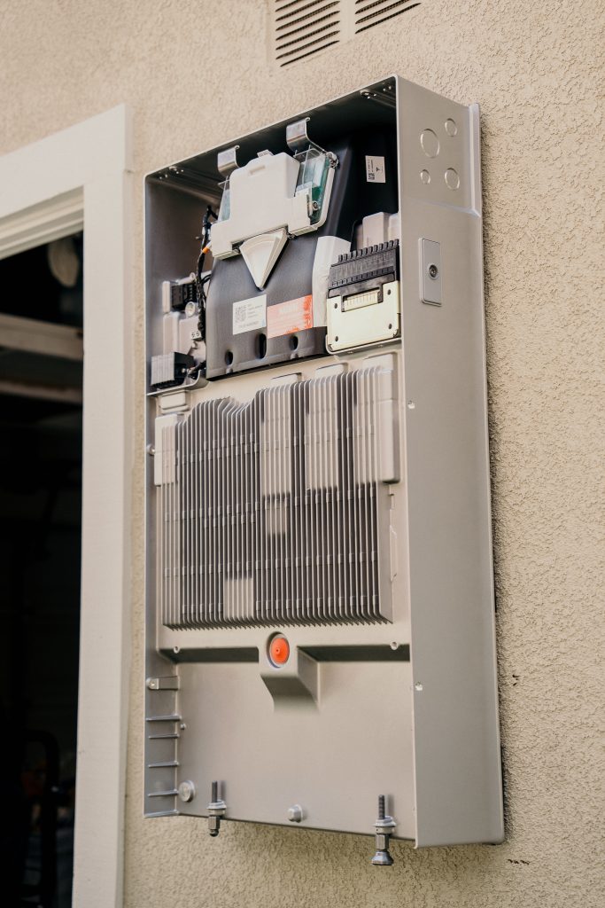 Bare whole-home backup battery being installed on the outside wall of a house